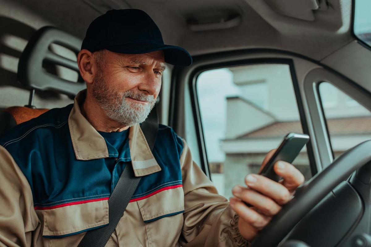 Medelålders man i arbetskläder sitter i tjänstebil och ser på sin mobil.